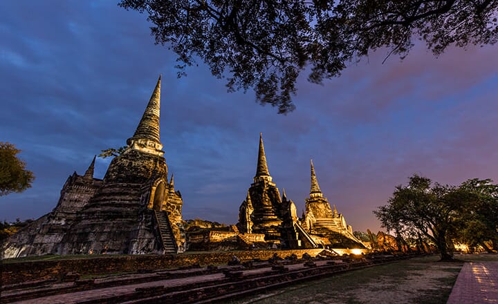 Stunning twilight view of Ayutthaya Historical Park, with ancient temple ruins lit by warm lights against a dusky sky.