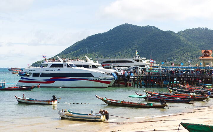 Lomprayah ferries docked at Mae Haad pier in Koh Tao, with traditional longtail boats in the foreground and a lush green mountain in the background